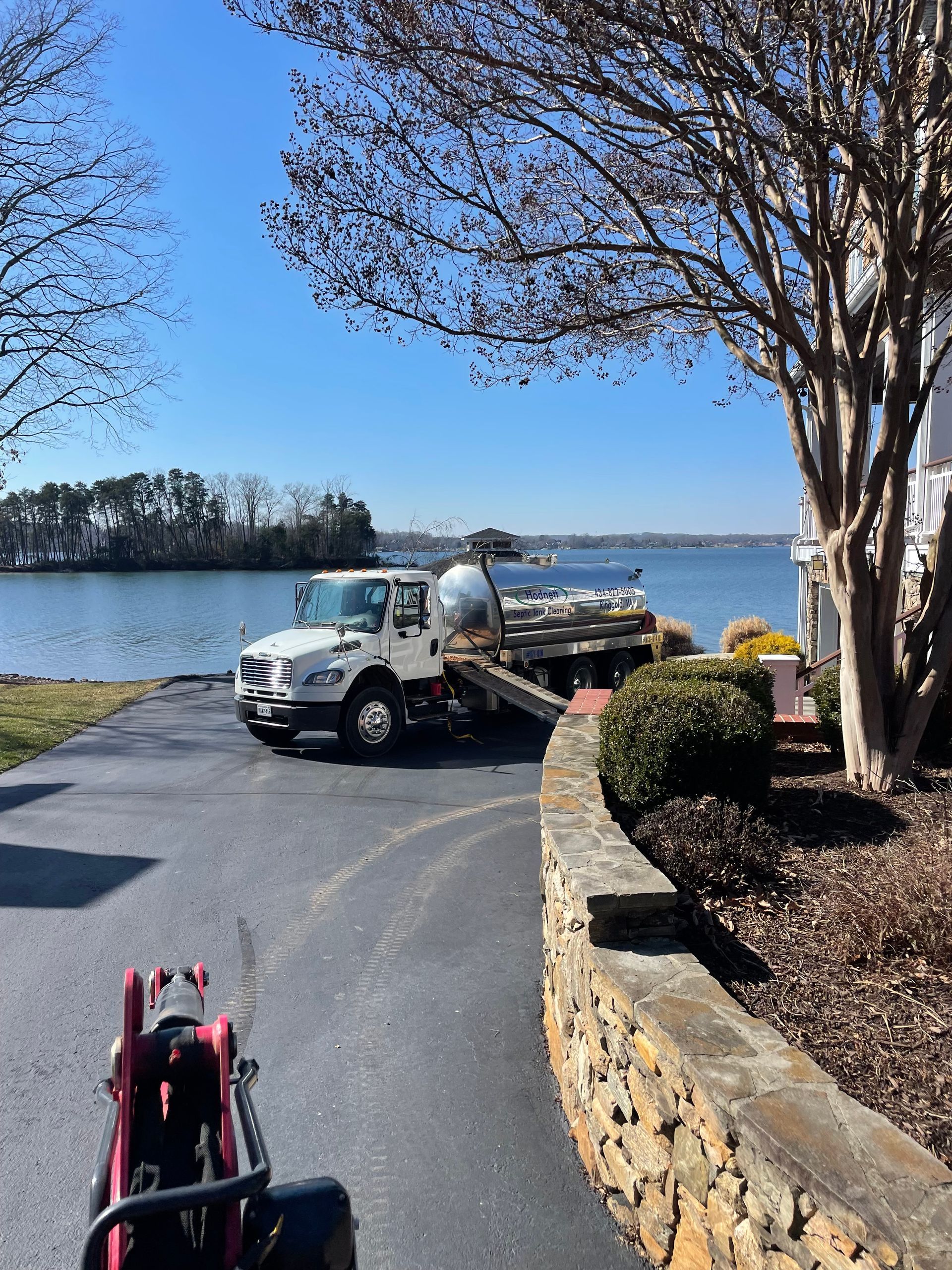 Truck parked near water, with a clear blue sky. Pathway, a wall, and greenery in foreground.