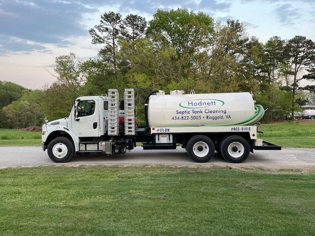 White septic tank truck on a paved road with green grass and trees; 