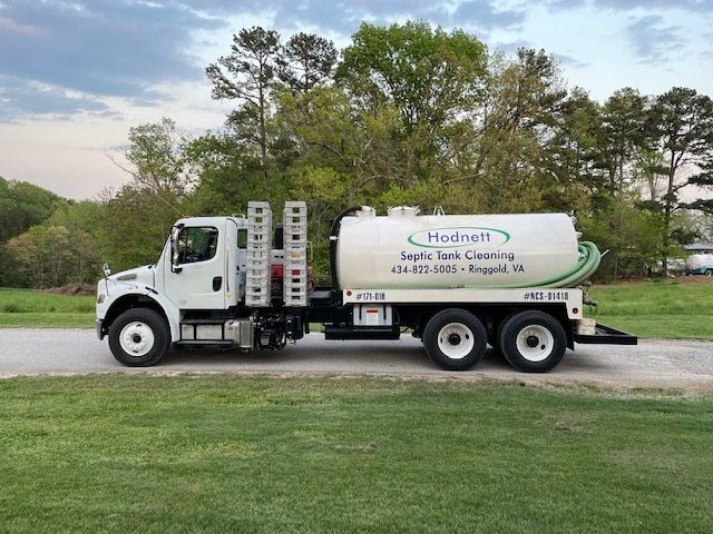 White septic tank truck on a grassy road, trees in the background; Hodnett Septic Tank Cleaning.