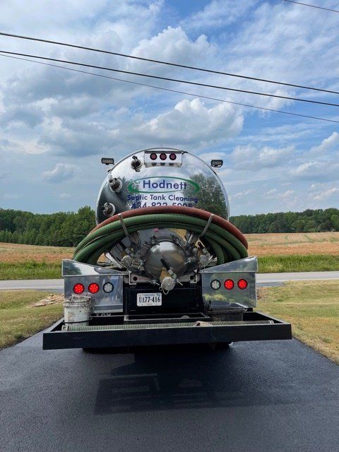 Rear view of a septic tank cleaning truck with a chrome tank and hoses. Green and red hoses, under a cloudy sky.
