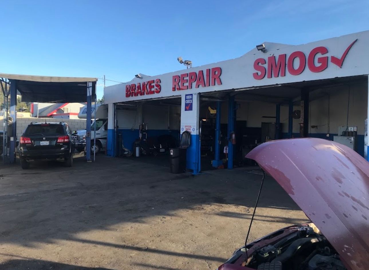 Auto repair and smog shop with cars under a canopy and a hood open in the foreground