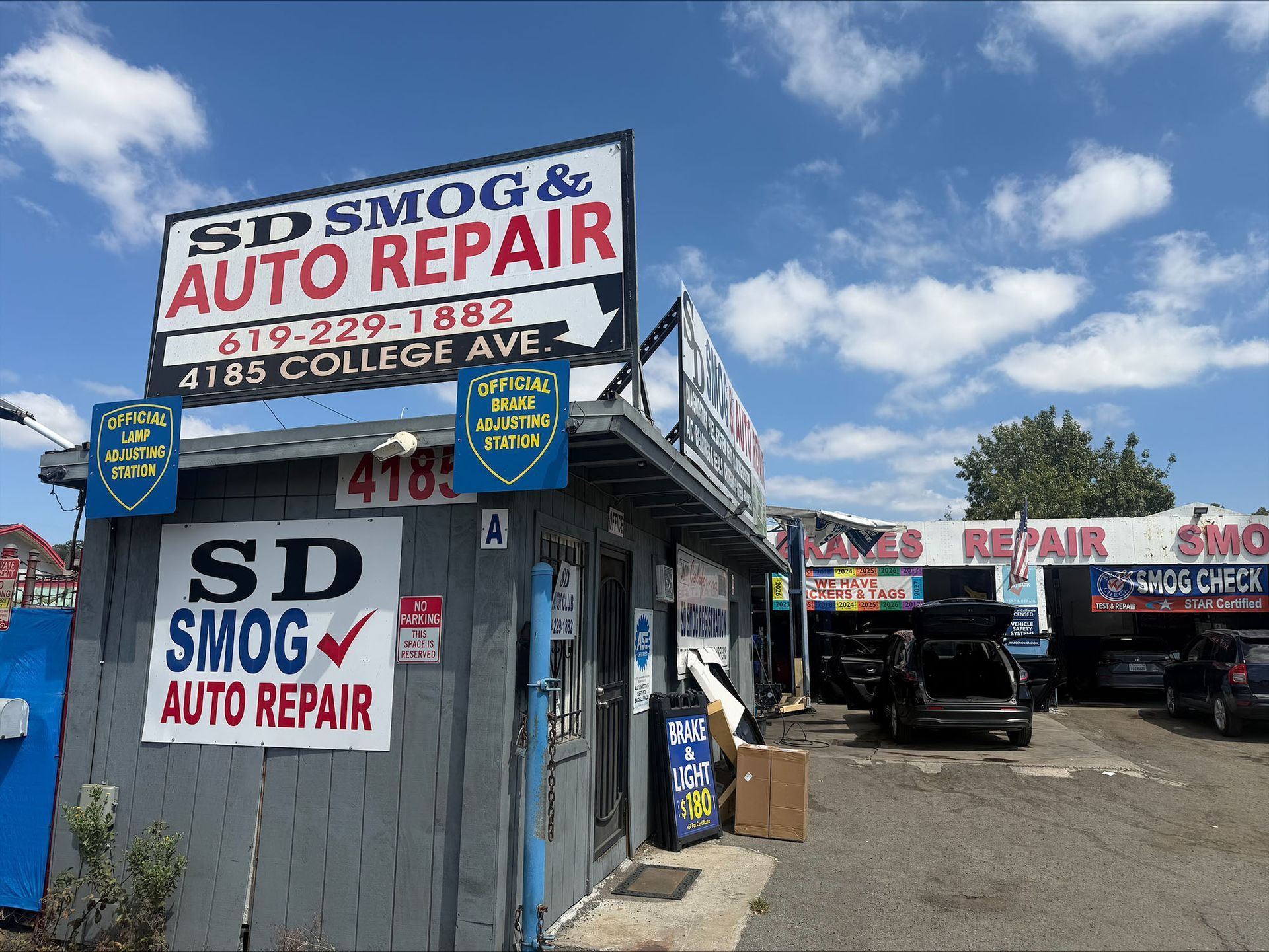 SD Smog & Auto Repair shop with cars and a tow truck under a blue sky