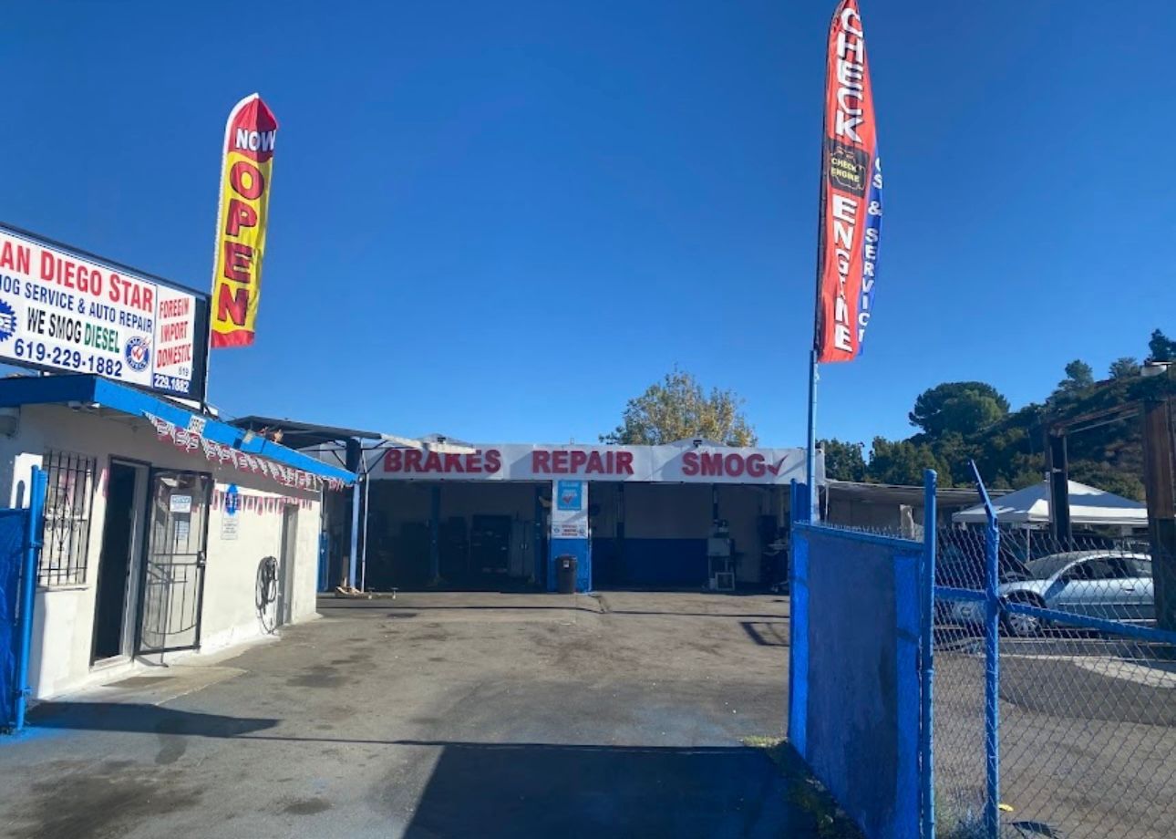 Auto repair shop exterior with blue gate, red signs, and parked cars under a clear sky