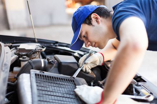 Mechanic in blue cap inspecting a car engine with tools in an auto repair shop