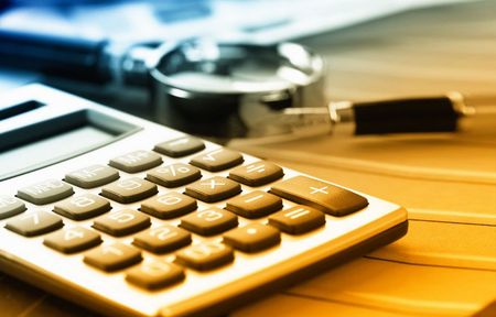 A calculator sits on a table next to a magnifying glass and a pen