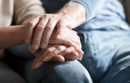 A woman is holding a man 's hand while sitting on a couch.