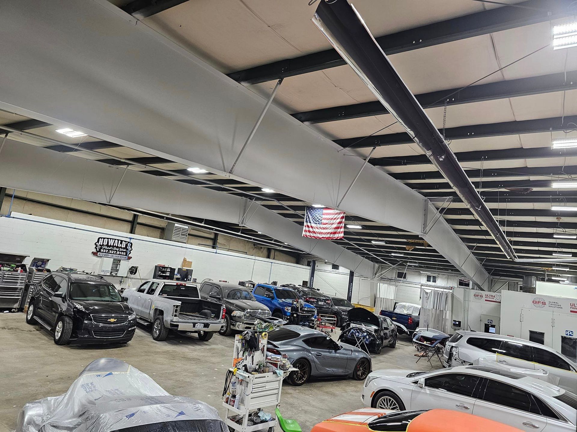 A lot of cars are parked in a garage with an American flag hanging from the ceiling.