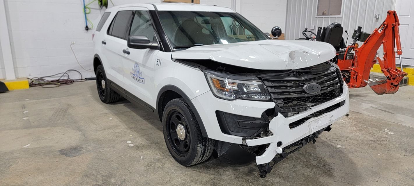 A white ford explorer with a damaged front end is parked in a garage