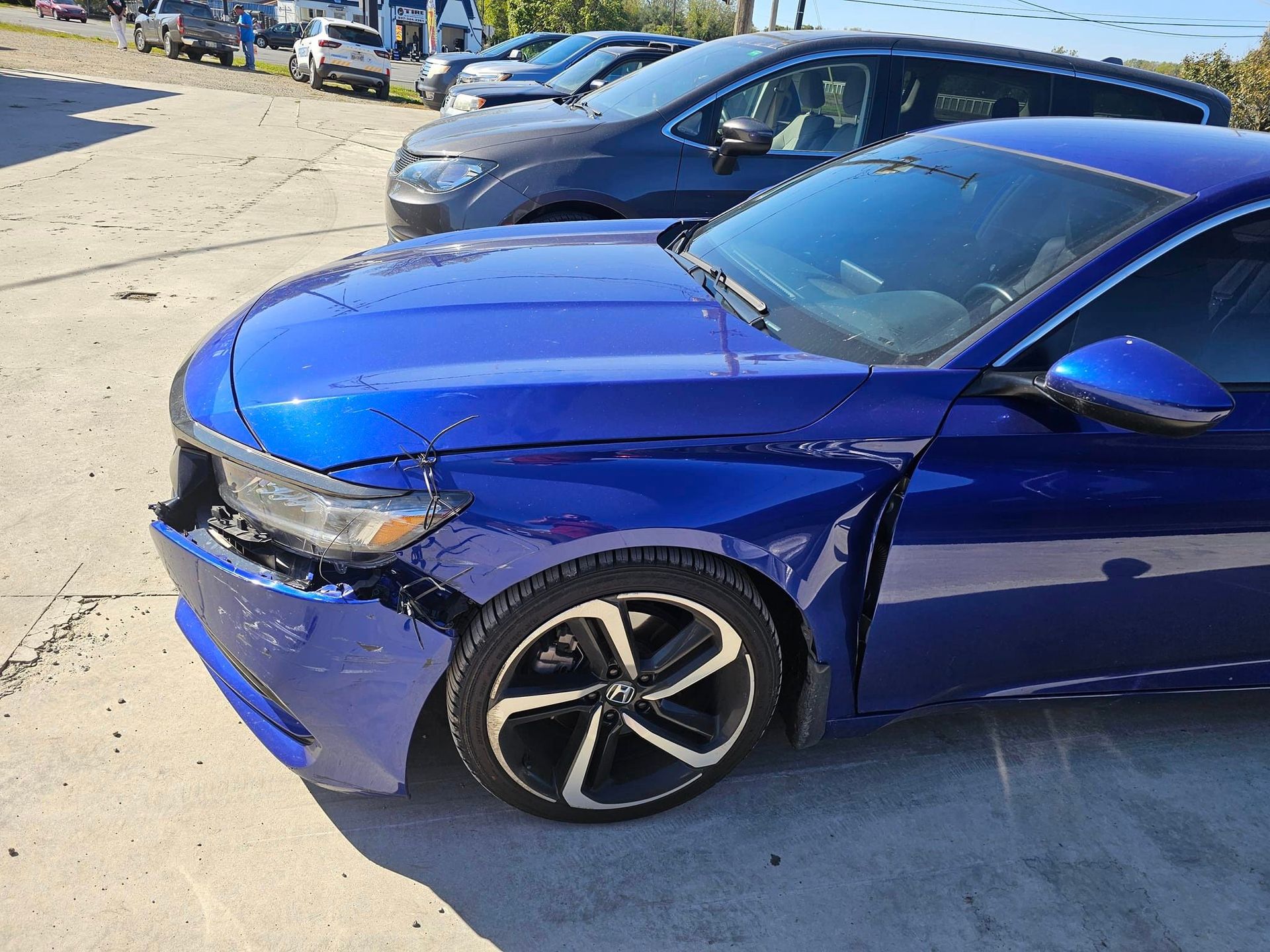 A blue car with a damaged Fender is parked in a parking lot