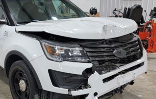 A white ford explorer with a damaged front end is parked in a garage