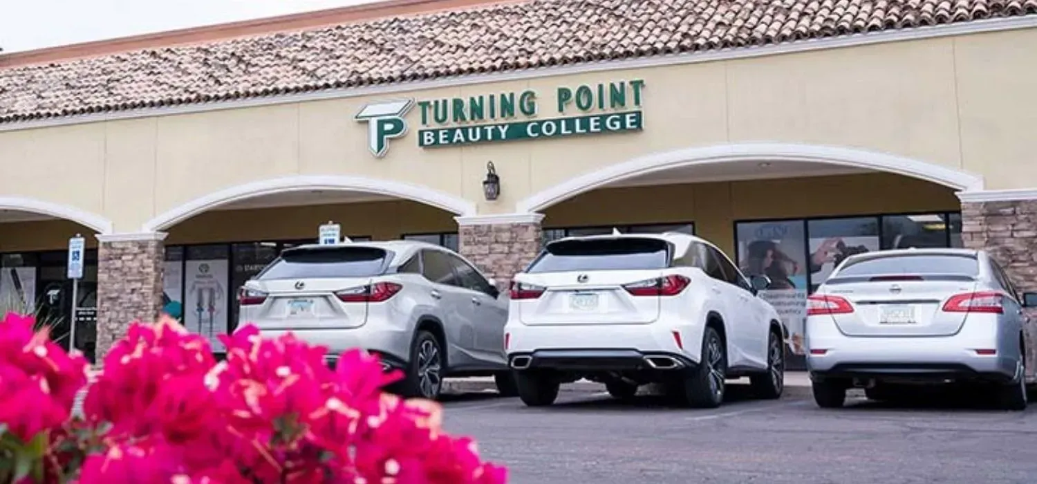 Exterior of Turning Point Beauty College with cars parked out front. Red flowers in the foreground.