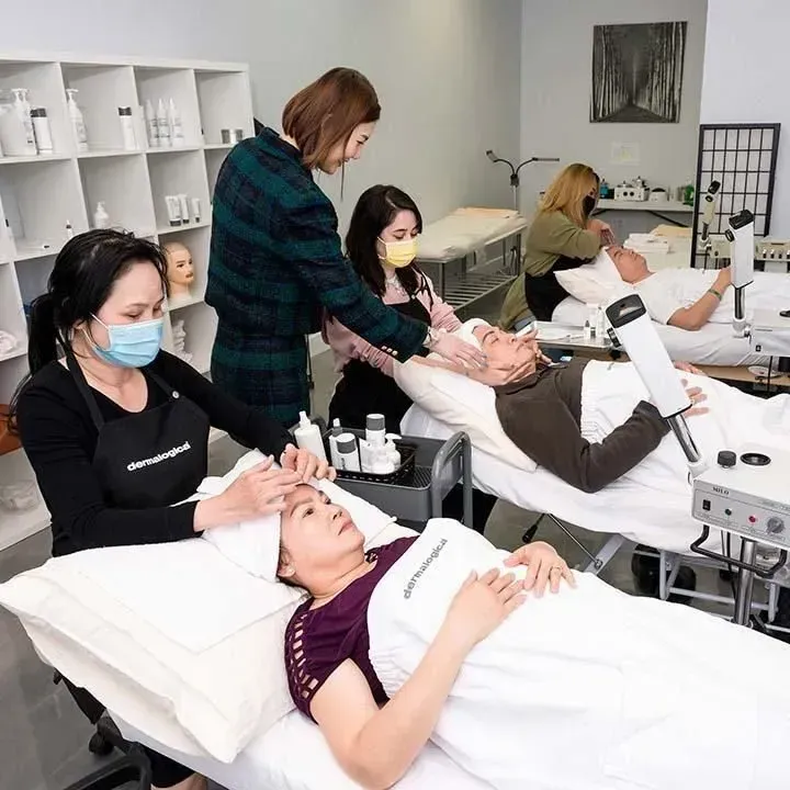 Esthetician students practice facials in a spa-like setting. Several students work on clients lying on beds.