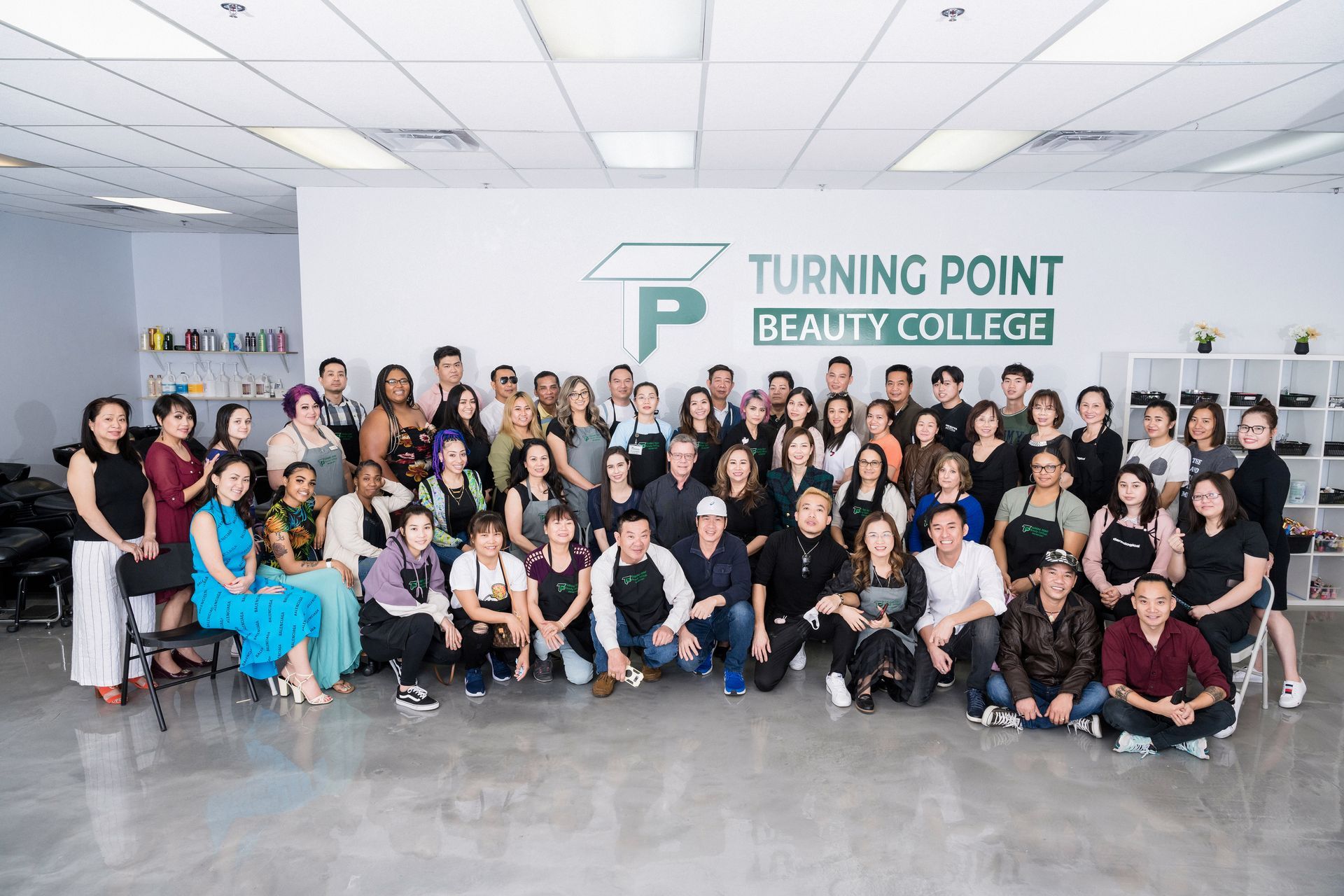 Group of people, Turning Point Beauty College, posing for a photo. Building interior, logo visible.