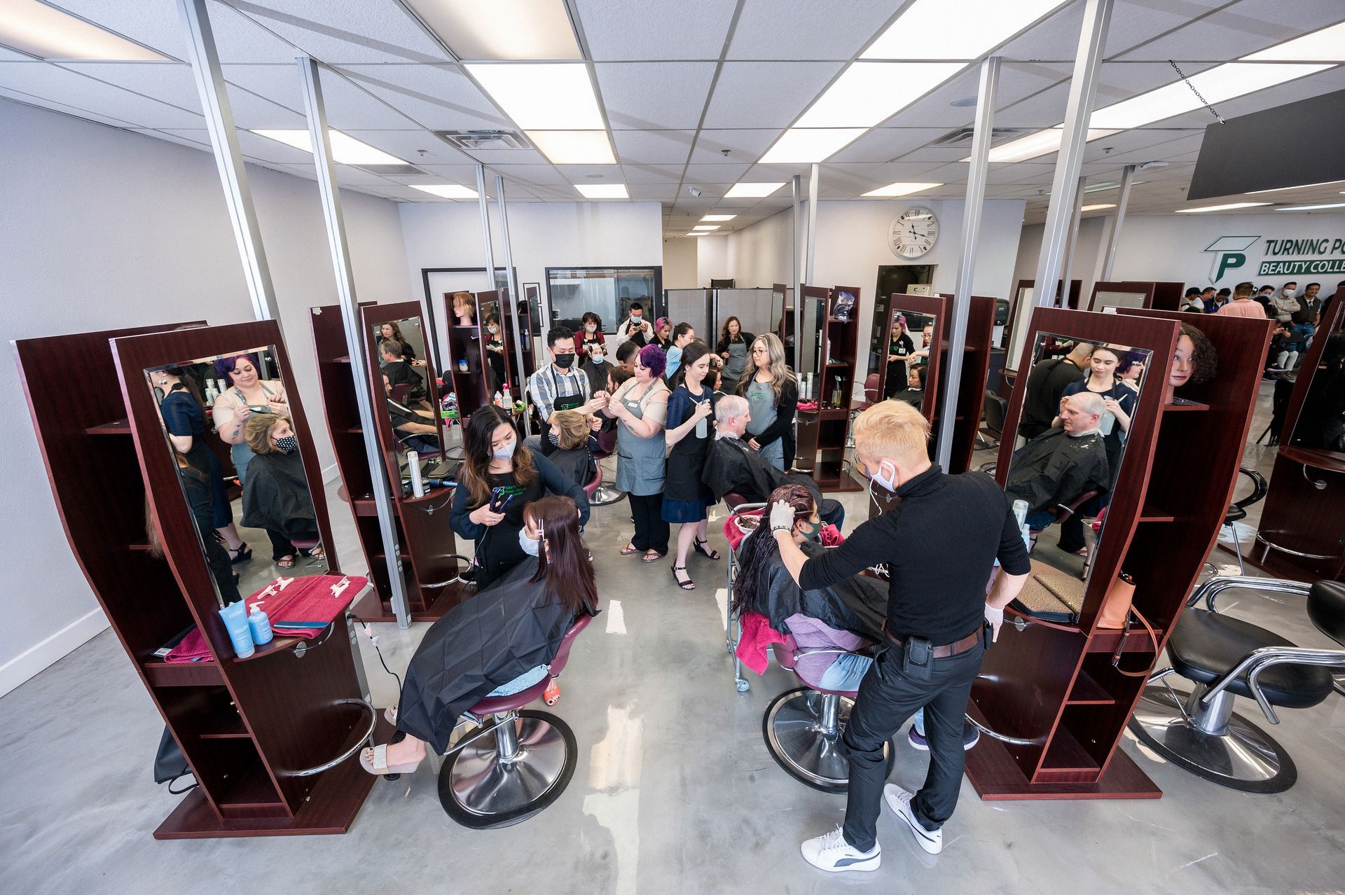 Hair salon with several stations, clients, and stylists. People are getting their hair cut.