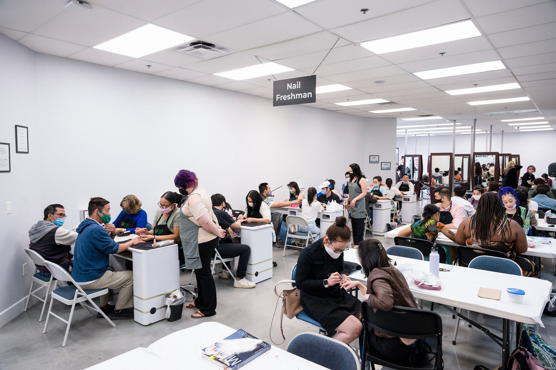A room with multiple people seated at tables, likely a nail salon or training setting.