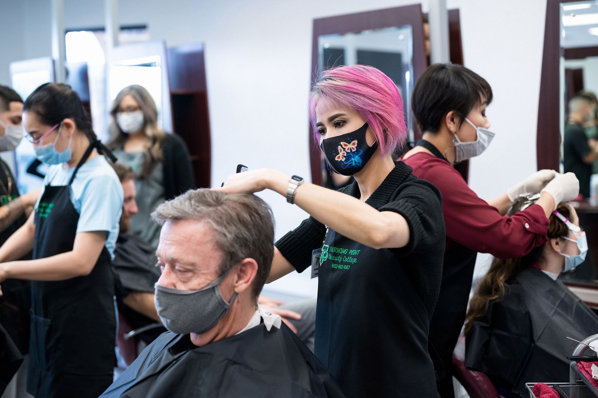 People at a hair salon wearing masks; stylists with clients getting haircuts and color.
