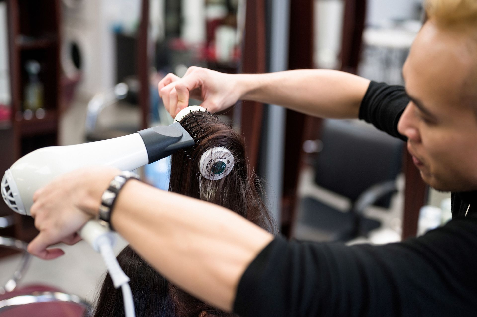 Hairdresser blow-drying a client's hair with a white hairdryer in a salon.