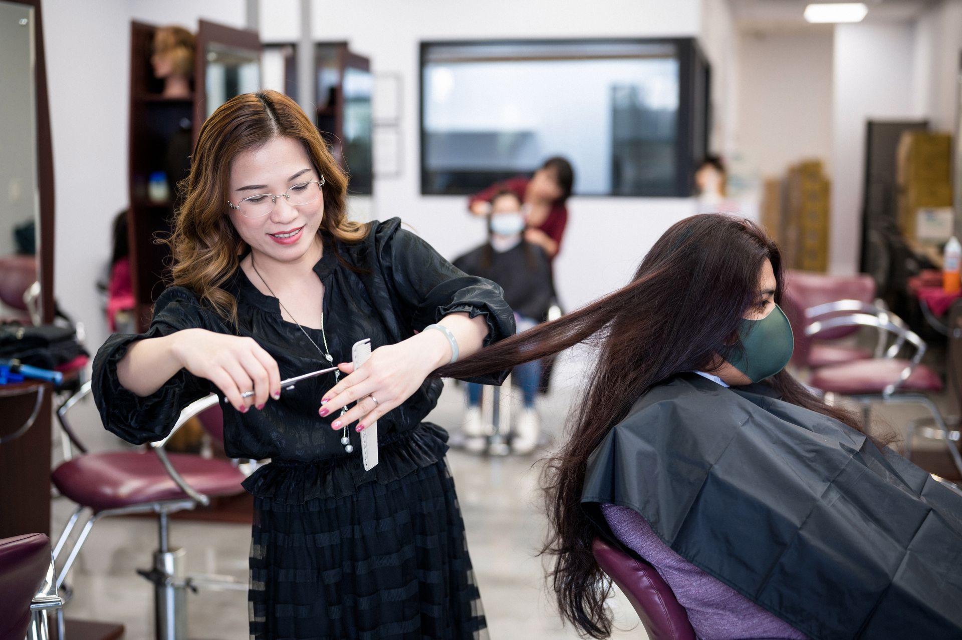 Hairdresser cutting a client's long hair in a salon. The client is wearing a cape.
