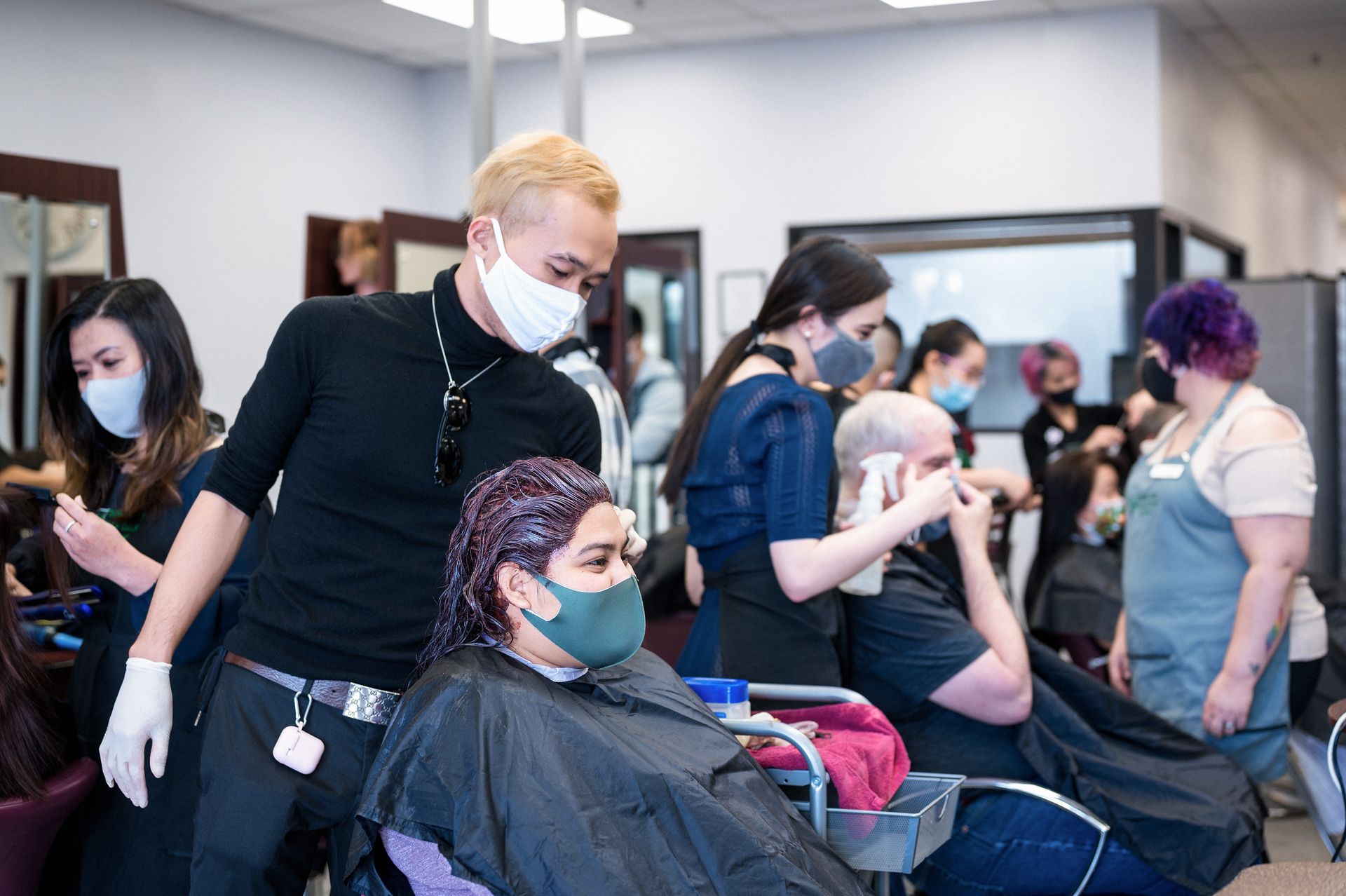 People with masks in a hair salon. Stylists work on clients' hair, wearing masks and gloves.