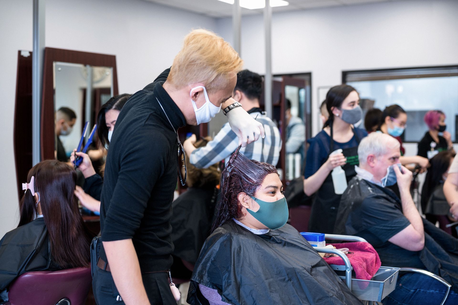 Hair stylists working on clients in a salon; people wearing face masks.