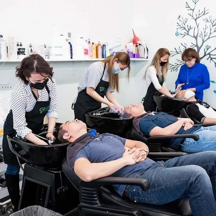 Hair salon: Four people getting their hair washed at washbasins by staff wearing face masks and aprons.
