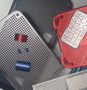 Stacked perforated plastic boards in gray and red with small blue and red parts on a tabletop.