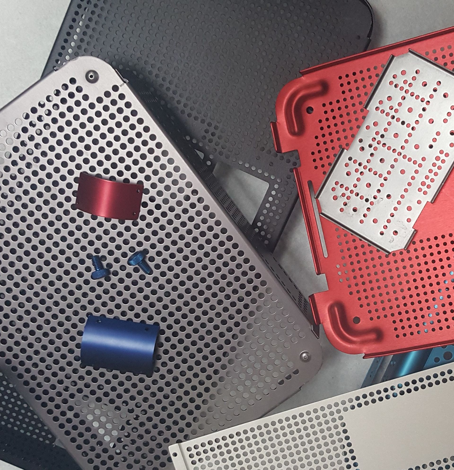 Stacked perforated plastic boards in gray and red with small blue and red parts on a tabletop.