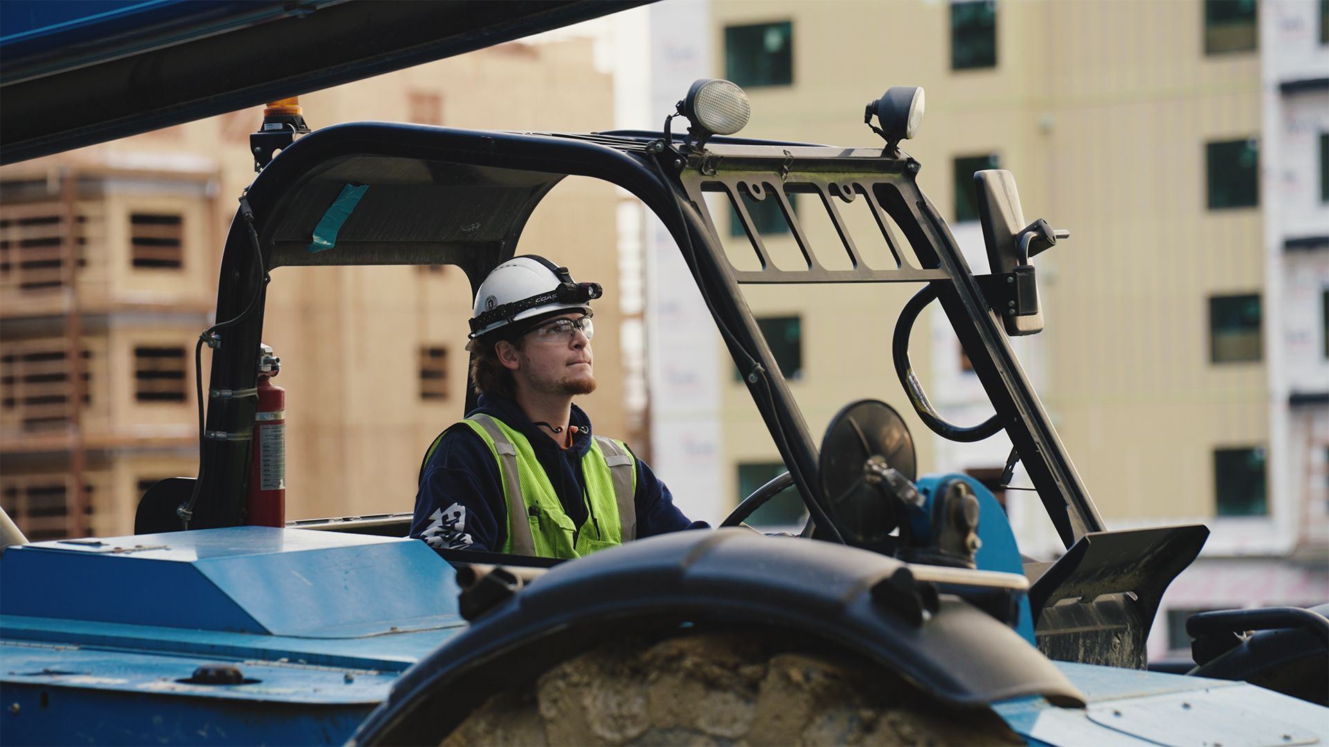 Construction worker in safety vest operating blue machinery at a building site