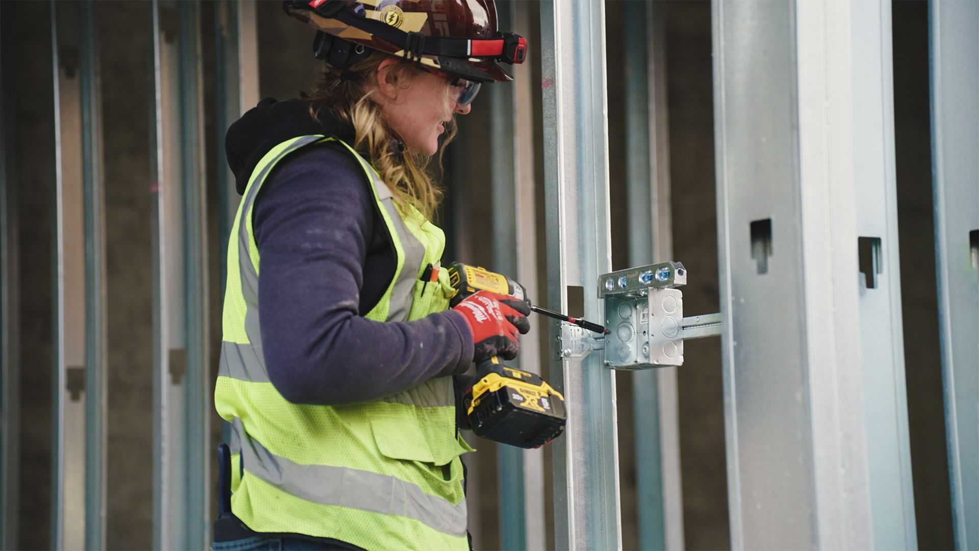 Construction worker in a safety vest and hard hat using a drill on a metal frame