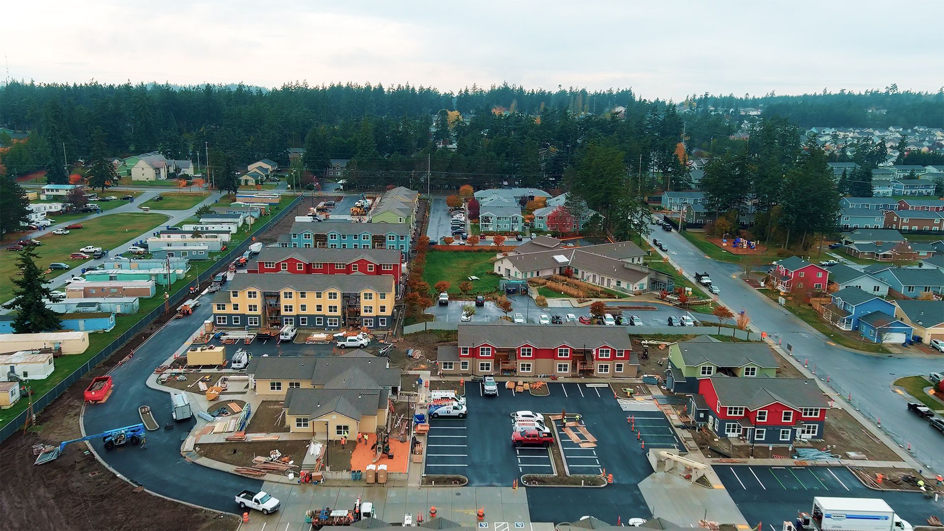Aerial view of a residential construction site with multiple buildings, trees, and parking areas