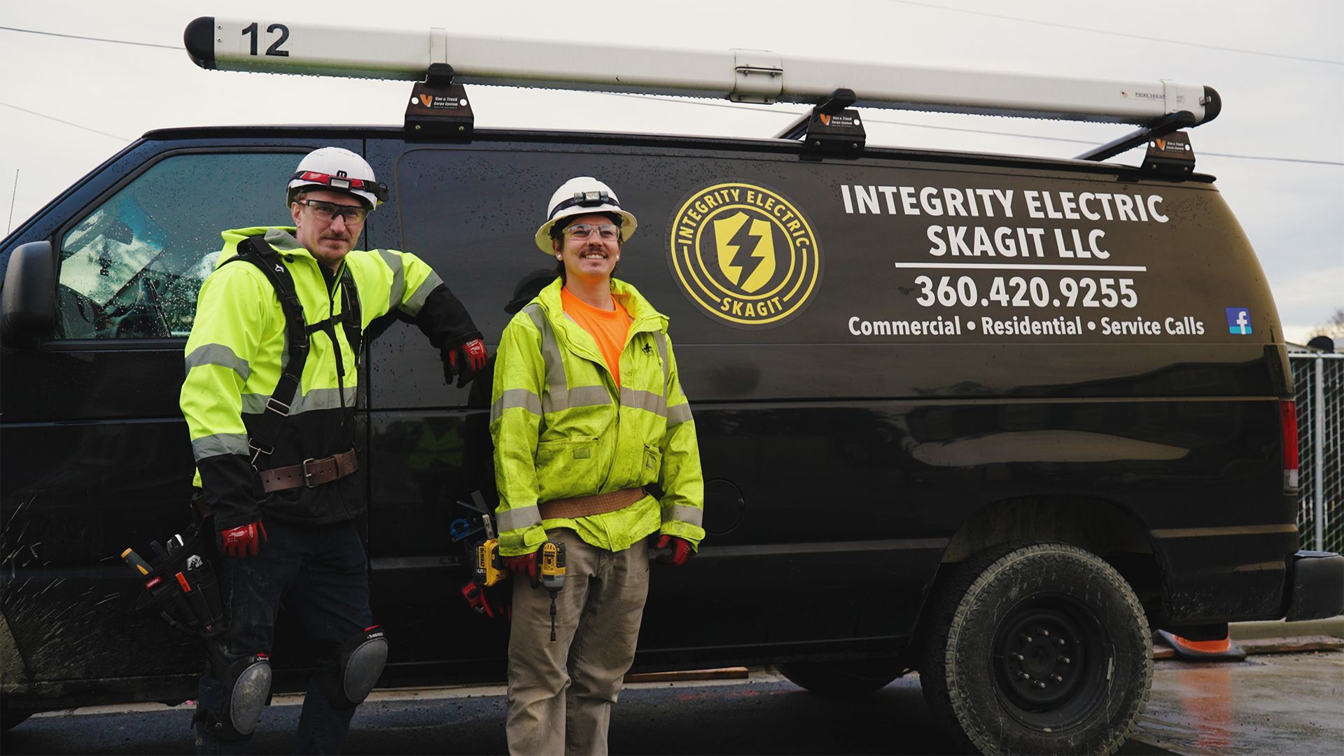 Two electricians in safety vests standing by a black work van 