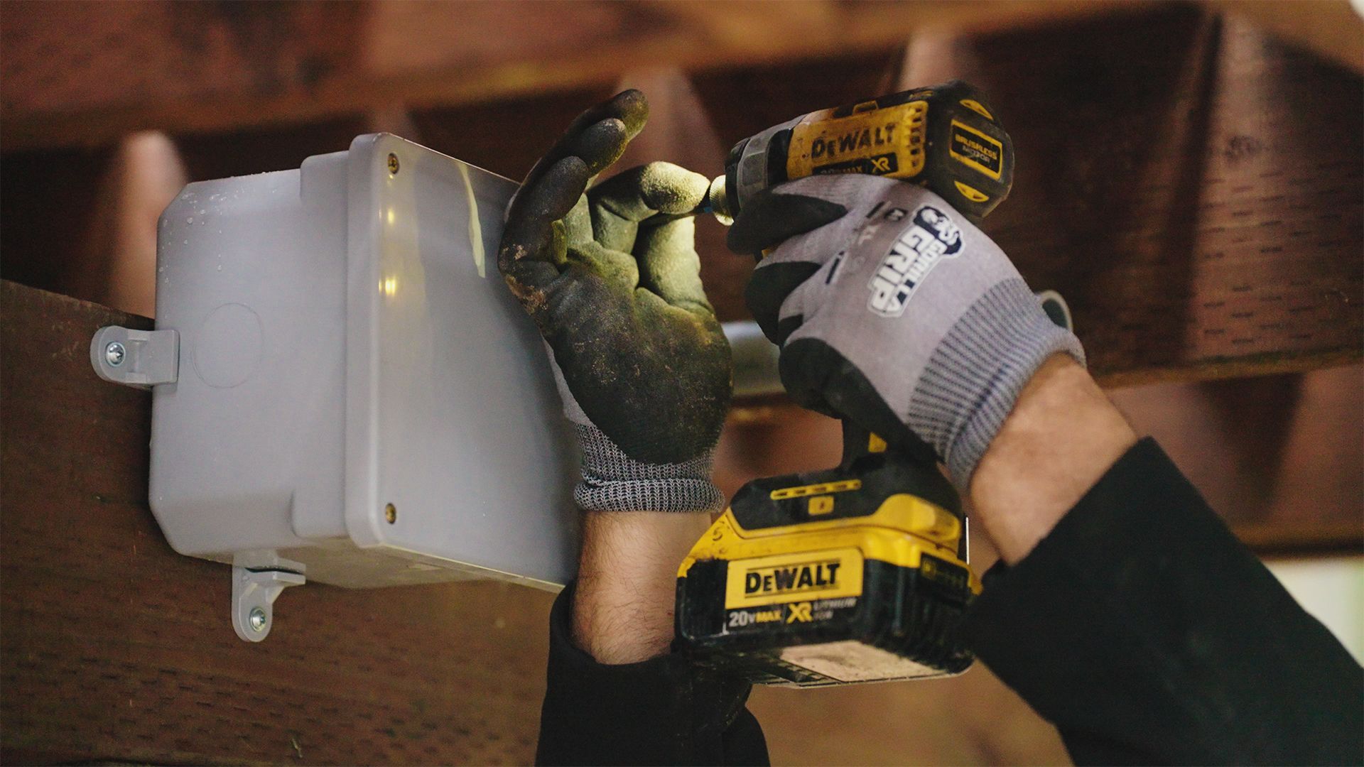 Person using a DeWalt drill to screw a box to a wooden beam