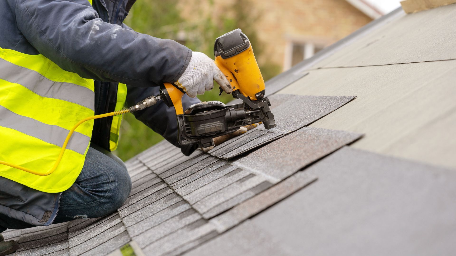 Worker using a nail gun to install roofing shingles on a sloped roof
