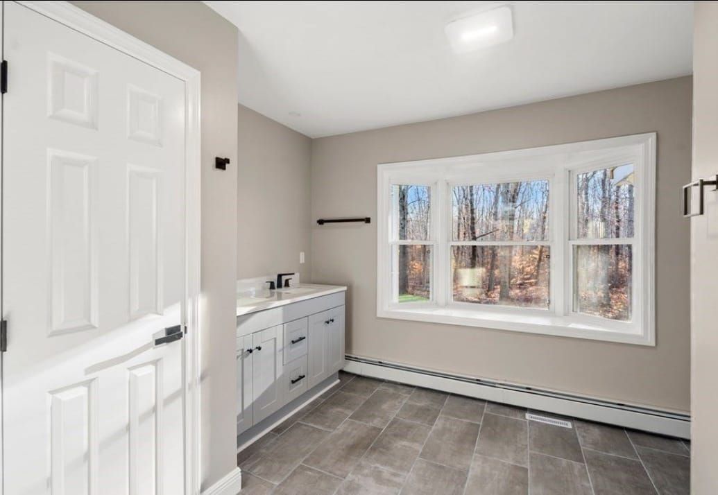 Bright empty laundry room with white cabinets, tile floor, and a window overlooking trees