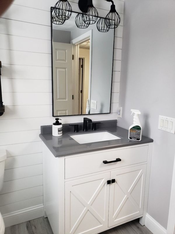 Bathroom vanity with gray countertop, black faucet, and mirror above white cabinet with X-style doors