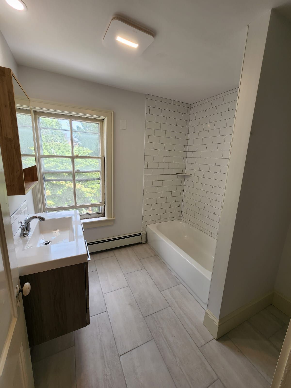Small bathroom with sink, window, bathtub, and light wood tile flooring