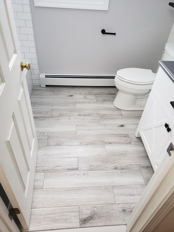 Small bathroom with light wood-look floor, white walls, toilet, vanity, and open door.