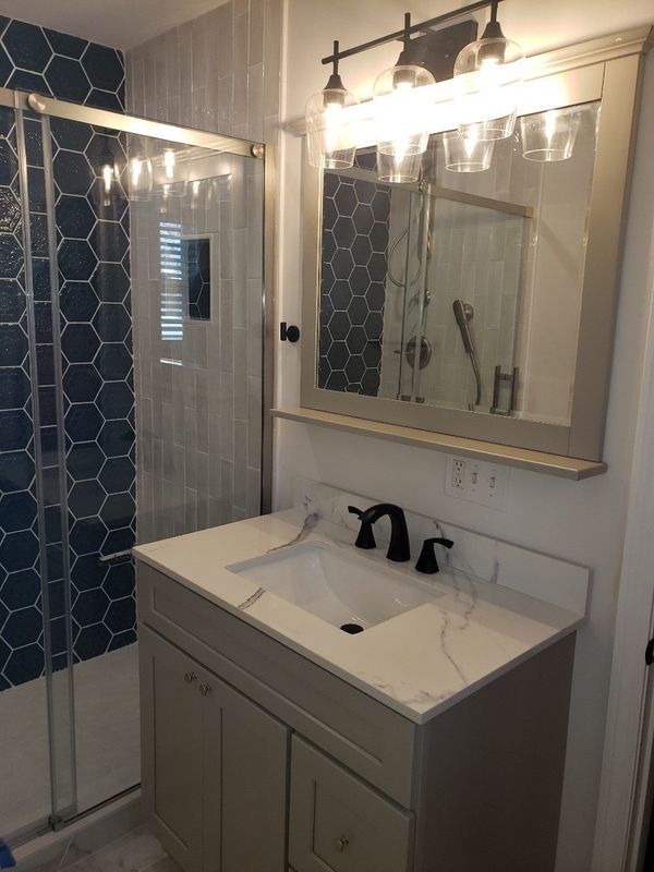 Small bathroom with vanity sink, mirror lights, and blue-tiled shower wall.