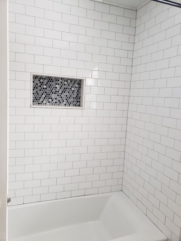 White tiled shower/tub alcove with a small mosaic recessed shelf/niche.