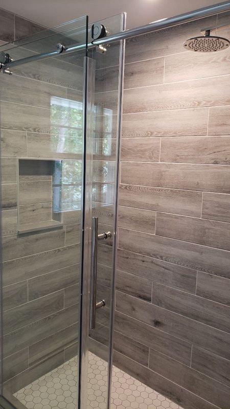 Glass walk-in shower with chrome fixtures, gray tiled walls, and a hexagon-tile floor.