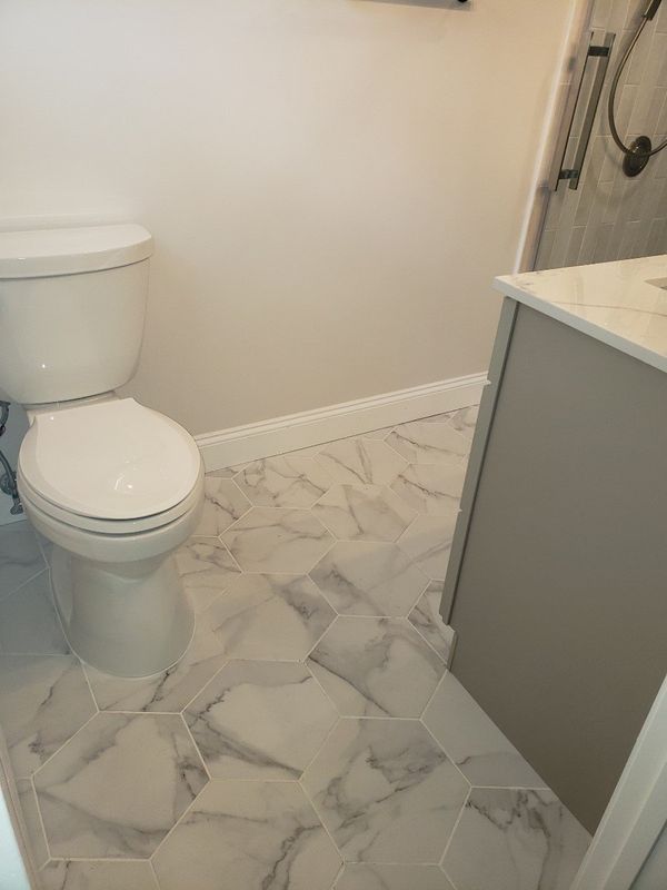 Small bathroom with white toilet, gray vanity, and marble-pattern tile floor