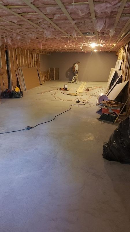 Unfinished basement with concrete floor, exposed ceiling joists, tools, and construction materials.