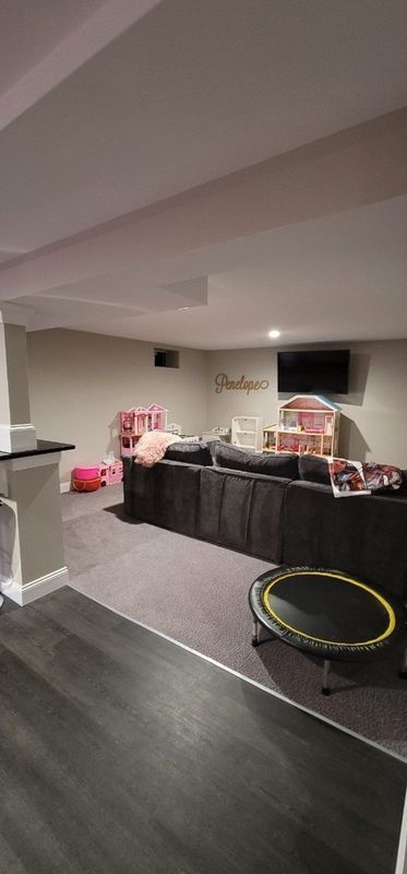 Basement living room with a gray couch, wall-mounted TV, and small trampoline on dark floor.