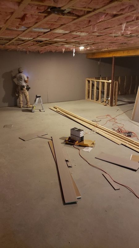 Basement under construction with unfinished ceiling, exposed framing, tools, and lumber on the floor