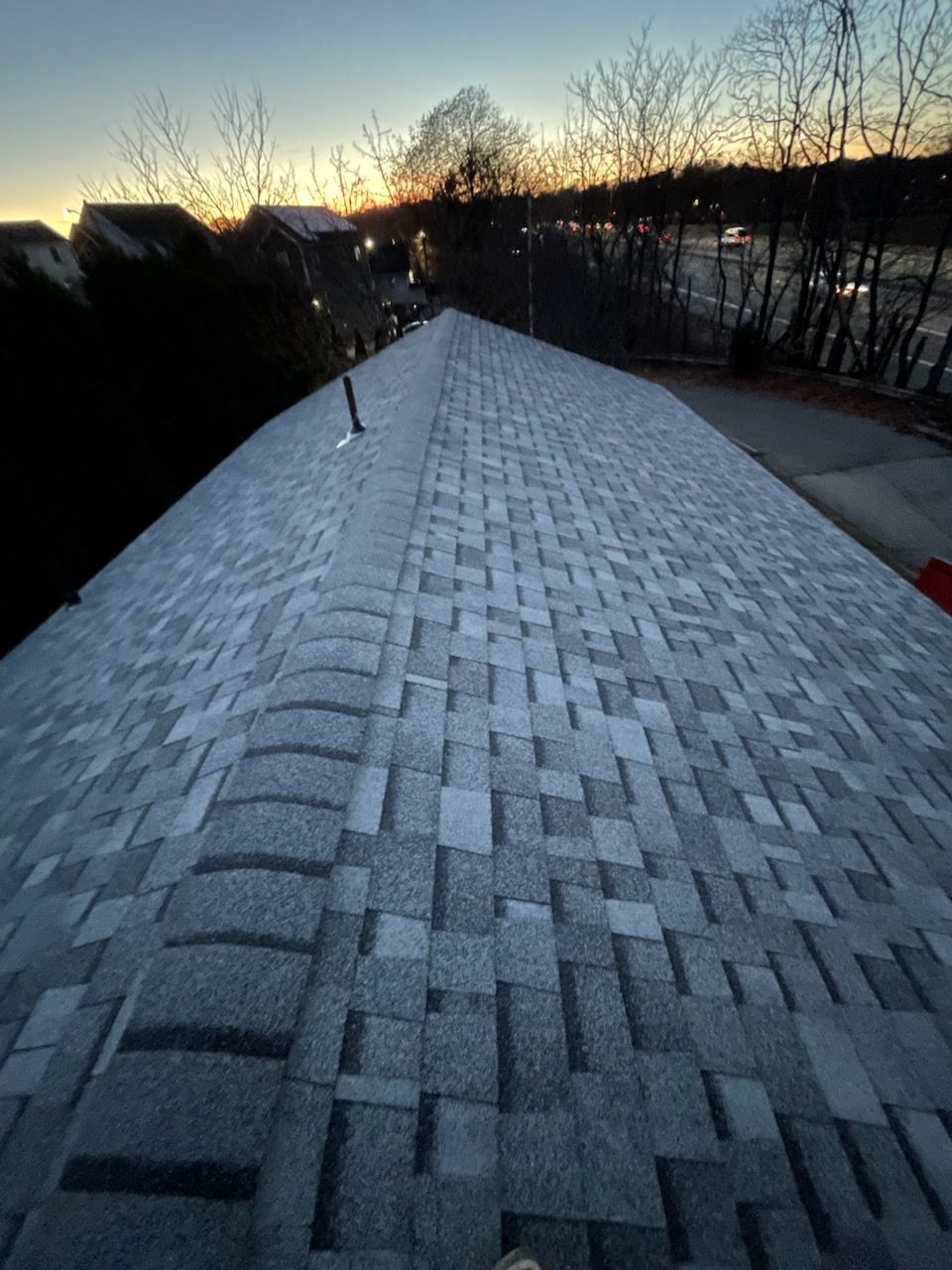Shingled rooftop at dusk with snow and leafless trees in the background