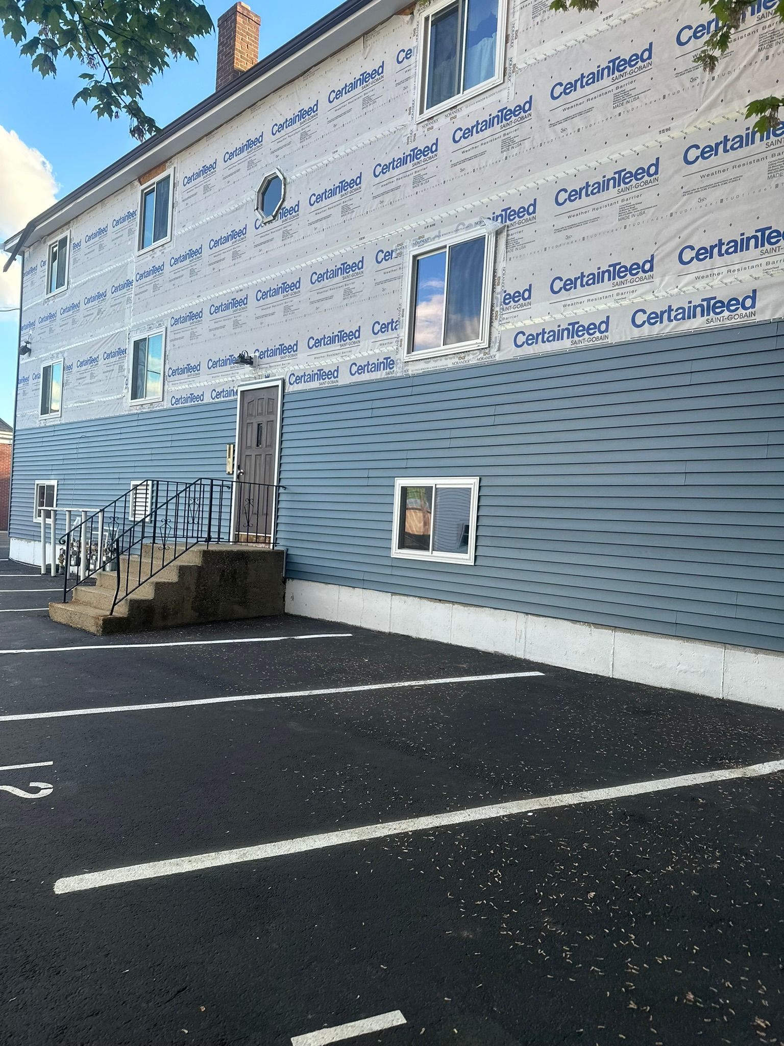 Building exterior wrapped in blue and white Tyvek, with a striped lower facade and parking lot in front