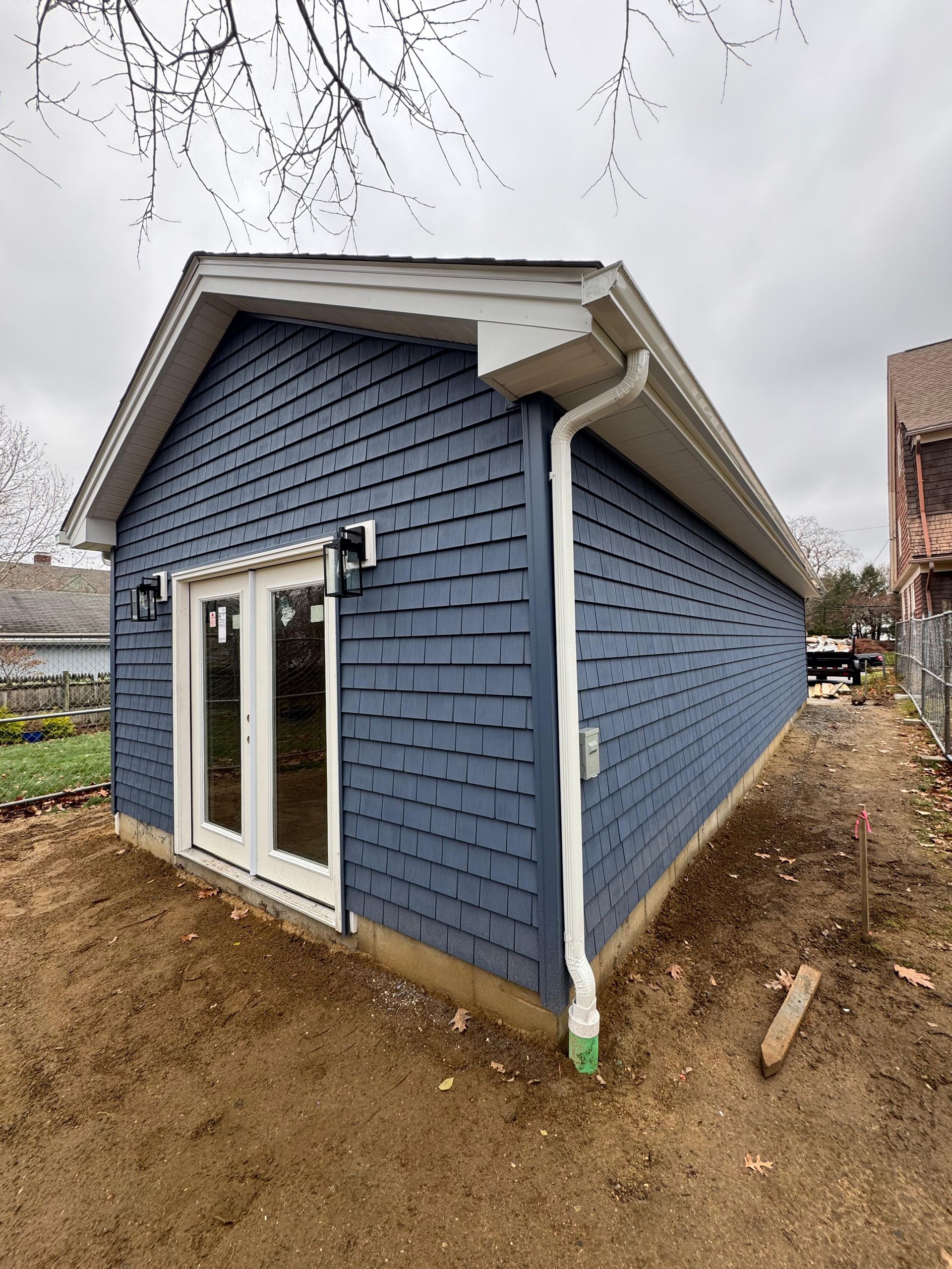 Small blue shed with white trim and double glass doors on a dirt lot