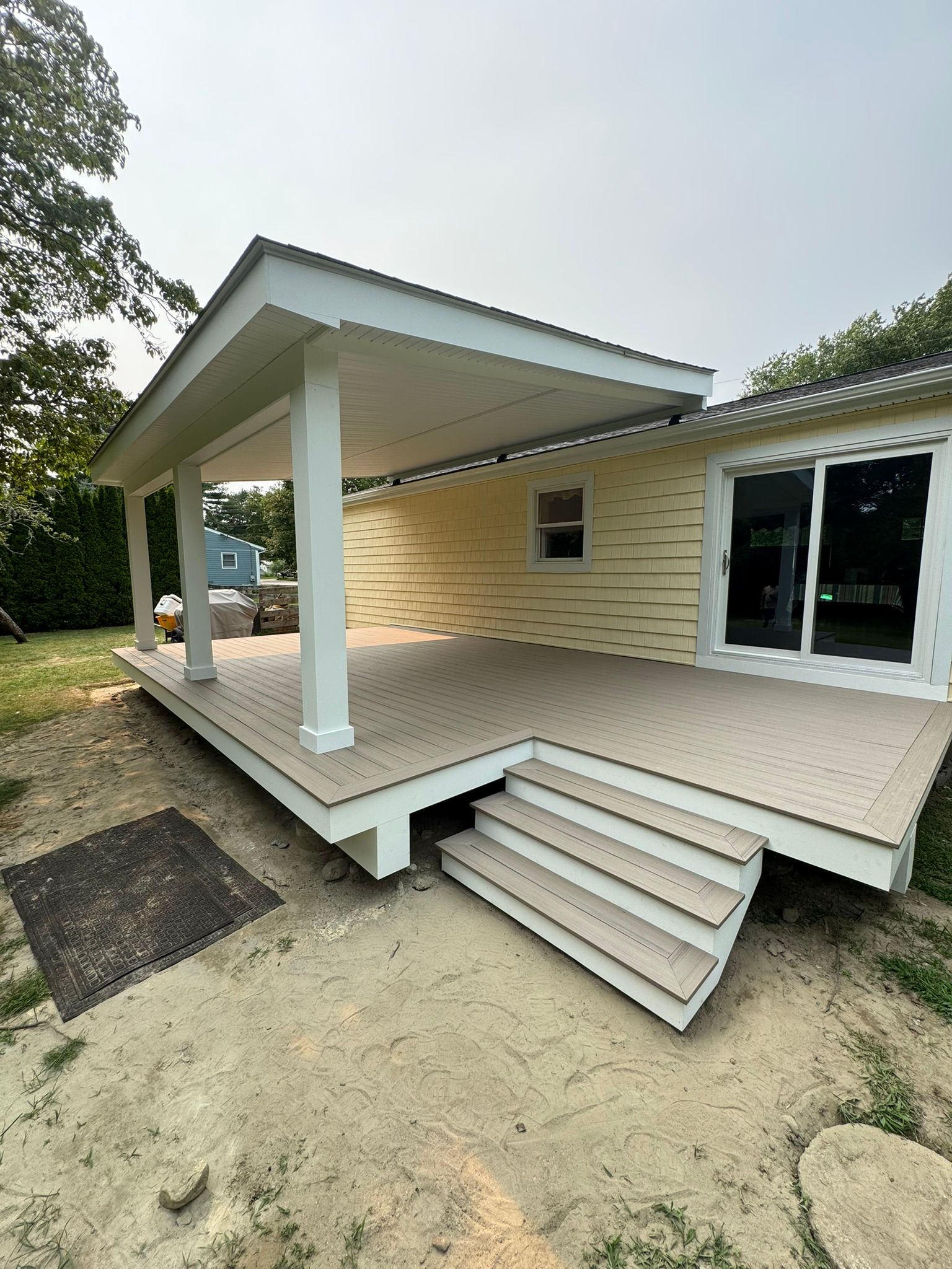 Front porch with ramp and steps on a light yellow house, with white columns and sliding glass doors.