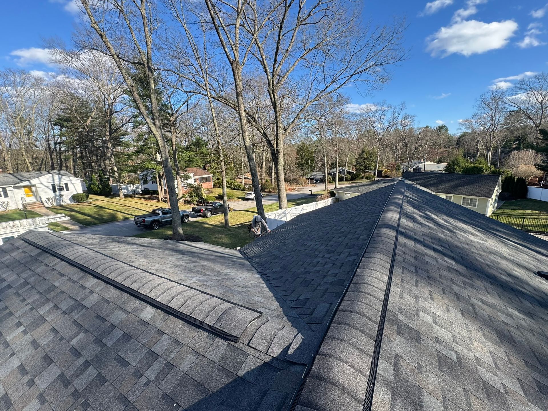 Rooftop shingles overlooking a residential neighborhood under a blue sky with bare trees