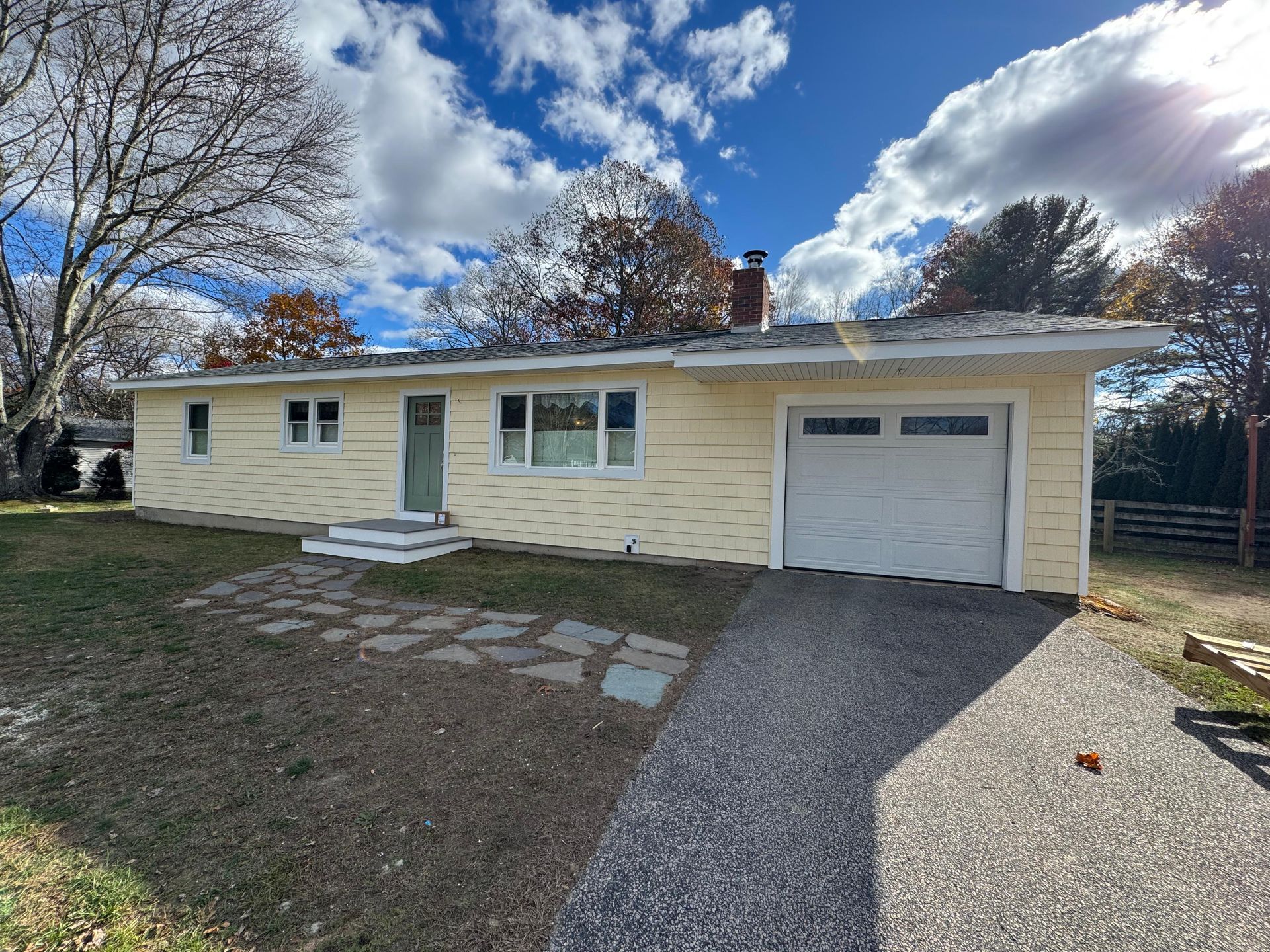 Single-story beige house with garage, gravel driveway, and stone path under a blue sky